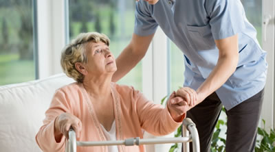 Elderly lady being help up to her walking support frame
